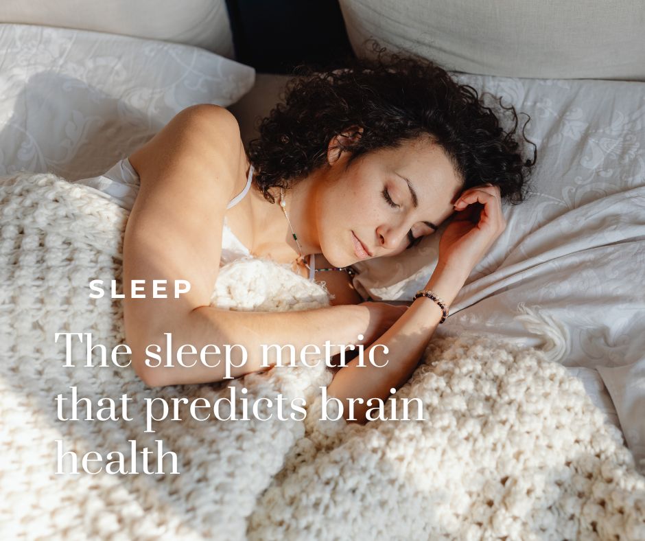 A woman with curly dark brown hair sleeps peacefully on her side in a bright, airy bedroom. She's wearing a light-colored tank top and resting on crisp white sheets and pillows, with a chunky cream-colored knit blanket draped over her. Soft natural light illuminates the scene, creating a calm, restful atmosphere. Text overlay in the lower left reads "SLEEP" in small caps above the headline "The sleep metric that predicts brain health" in a white serif font.